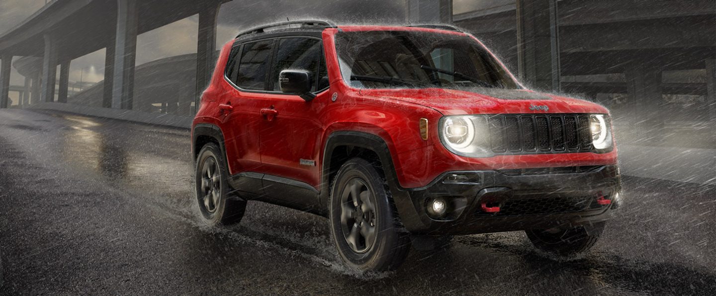 A red 2021 Jeep Renegade being driven through a rainstorm with its headlamps on.