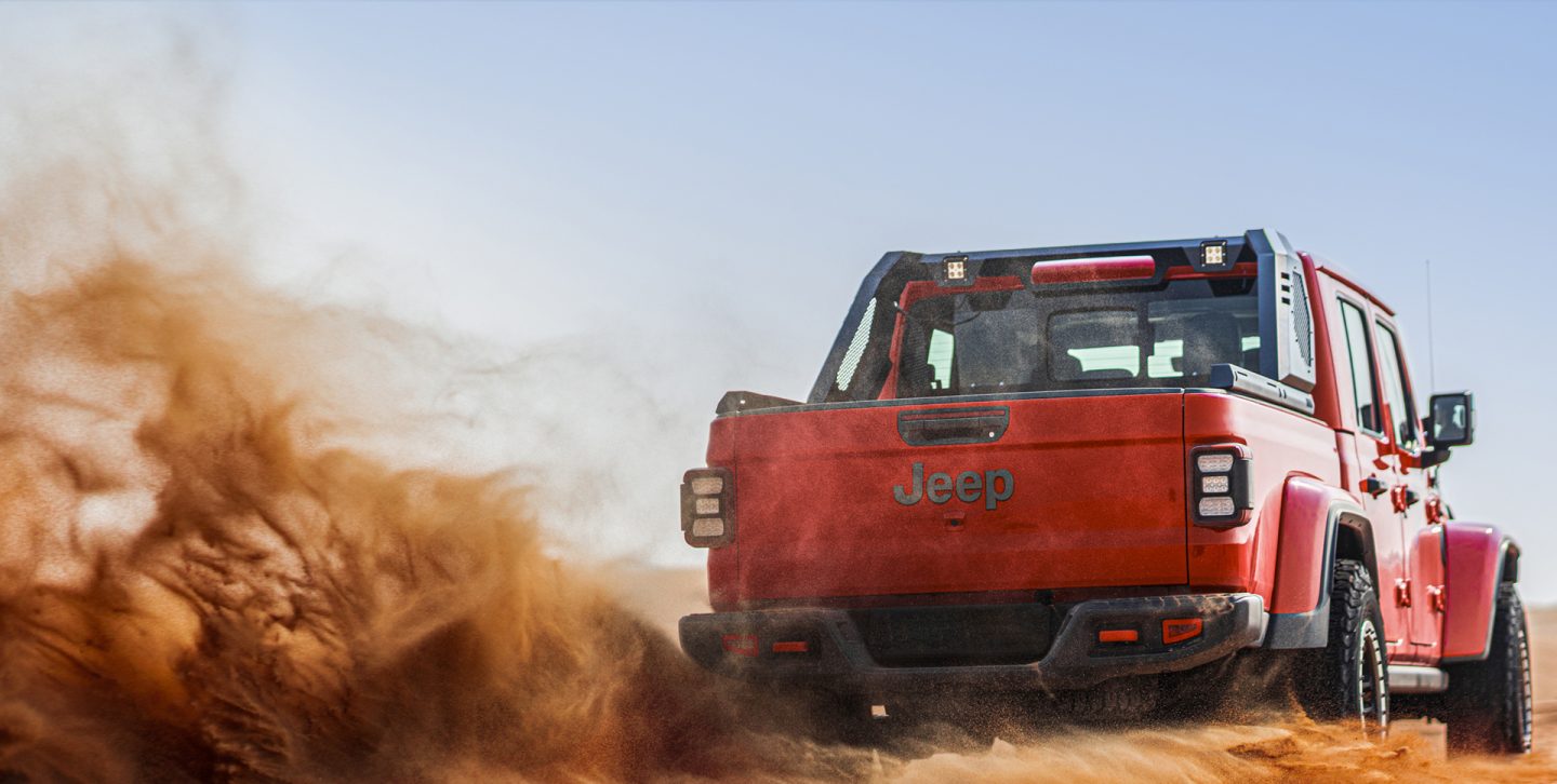 A 2022 Jeep Gladiator Overland being driven on a highway as it tows another vehicle on a flatbed trailer.