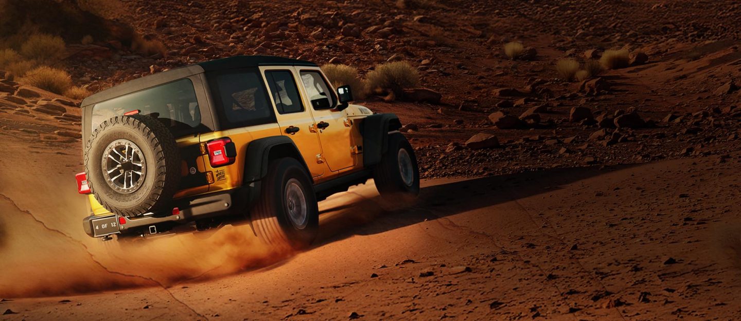 A passenger-side rear angle of a gold 2026 Jeep Wrangler Willys 392 with a black top, traveling on a sandy trail, off-road in the desert.