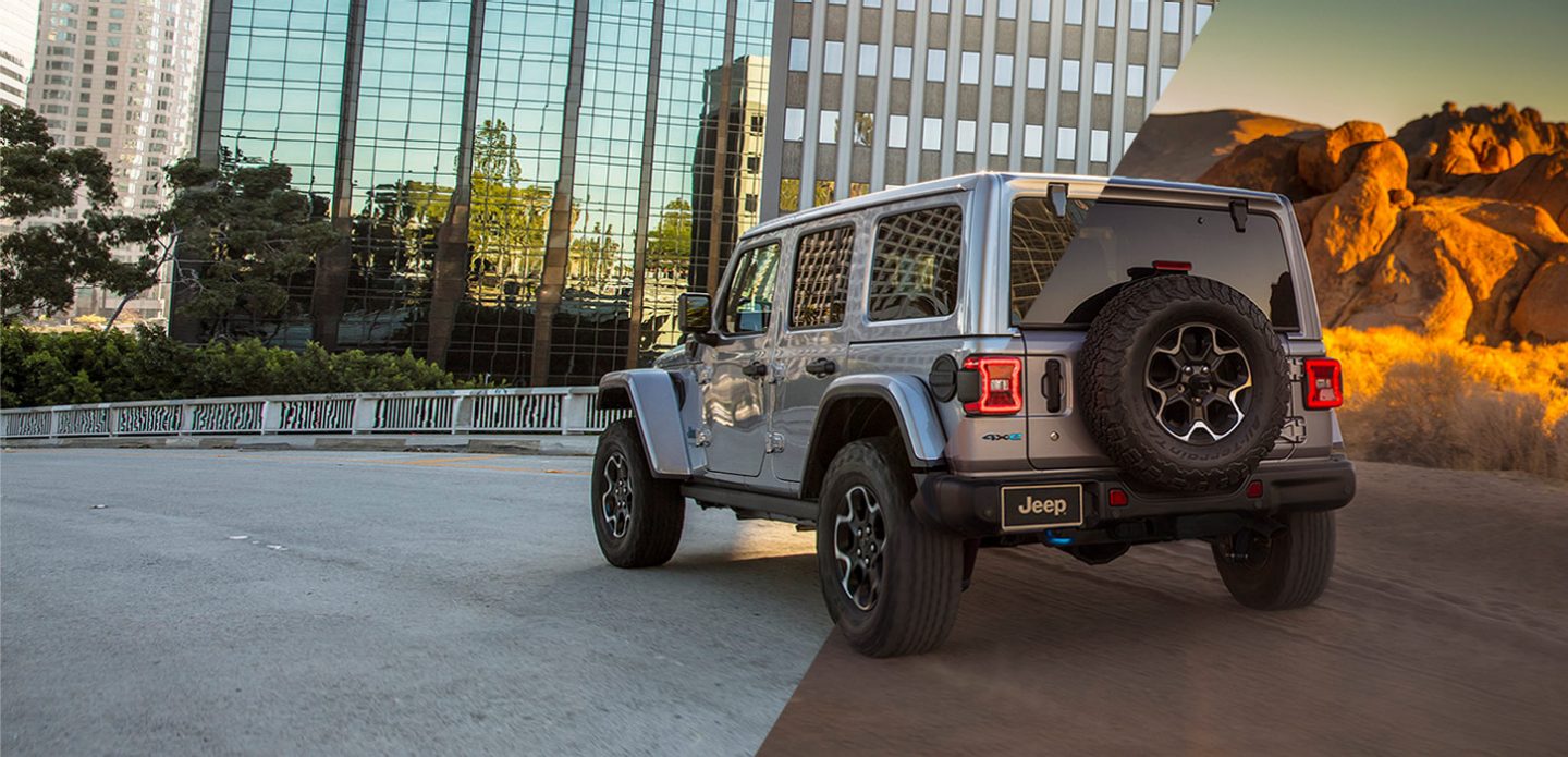 Three-quarter rear view of a 2021 Jeep Wrangler 4xe with a split-screen background: skyscrapers on the left, mountains on the right.