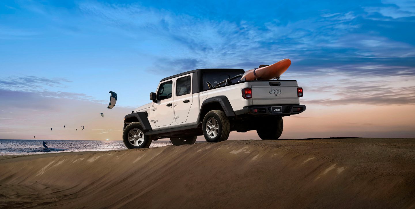 The 2022 Jeep Gladiator Rubicon with its doors off and windshield folded down, parked on a rocky beach.