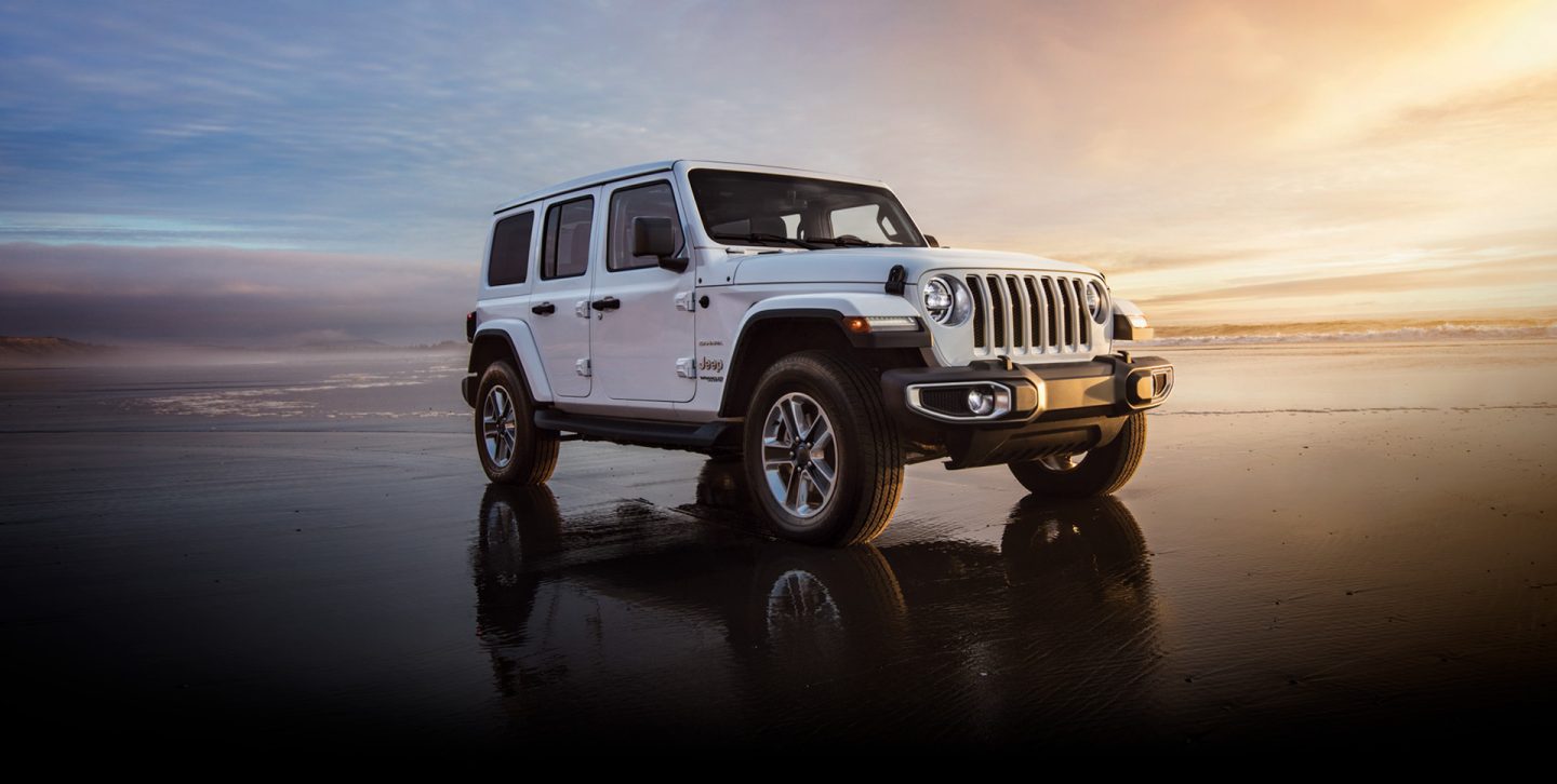 The 2022 Jeep Wrangler Sahara parked on a beach in shallow water.
